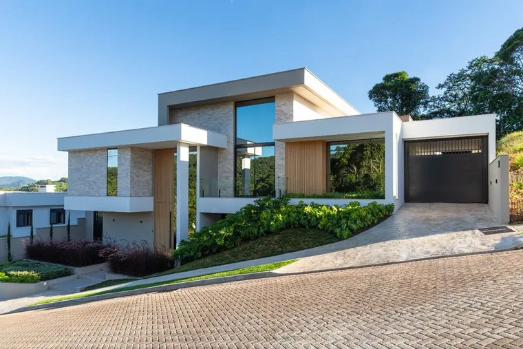 Casa JG vista da rua em diagonal, com a rampa de acesso à garagem e o jardim no talude