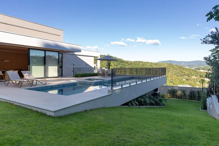 Área da piscina da Casa JG com deck, gramado e vista para os morros